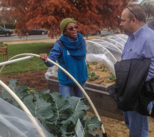 Farmer and customer talking in front of greenhouse full of leafy green vegetables