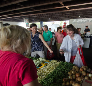 woman smiling while shopping at a busy farmers' market