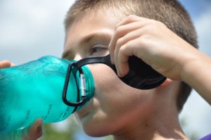 Child drinking from blue refillable water bottle, outdoors.