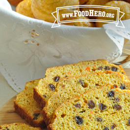 sliced sweet carrot bread on a cutting board next to a basket of sweet carrot muffins