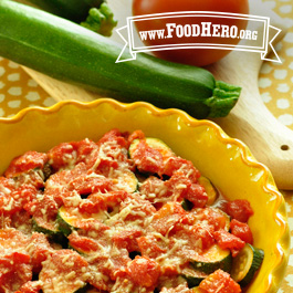 a dish of zucchini zowie next to fresh zucchini and tomato on a cutting board