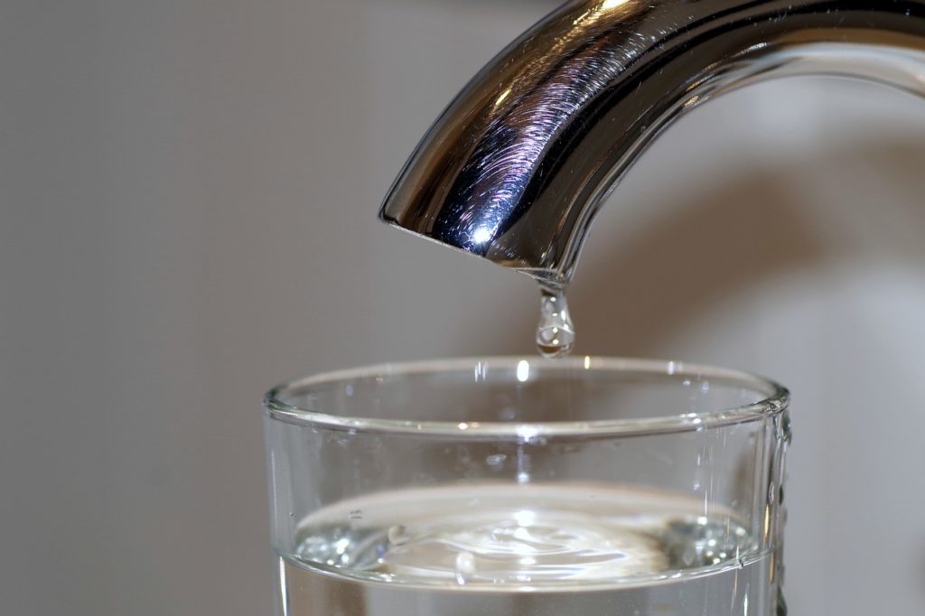 Glass of water being filled from a faucet.