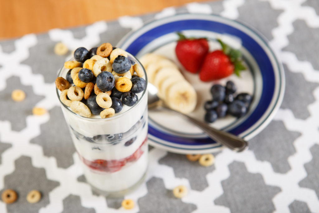 yogurt berry parfait in a parfait glass next to a plate of sliced fruit