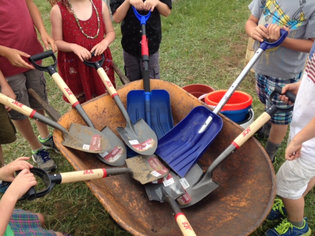 group of young gardeners gathering their shovels inside a wheelbarrow to celebrate their teamwork