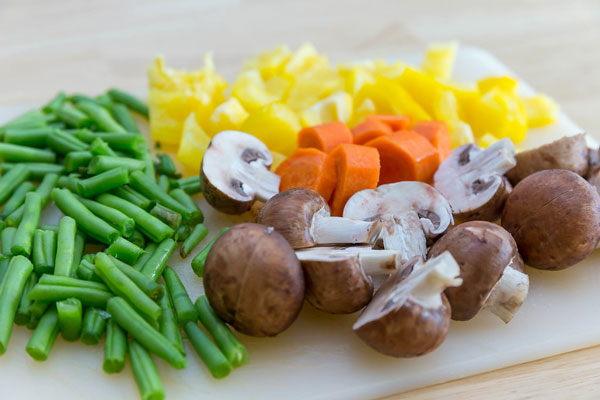 cutting board with sliced green beans, yellow pepper, carrot, and mushrooms
