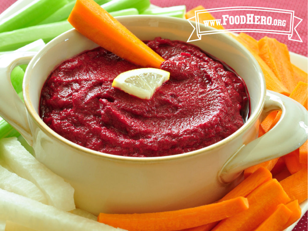 beet dip in a bowl surrounded by fresh cut carrots, celery and squash
