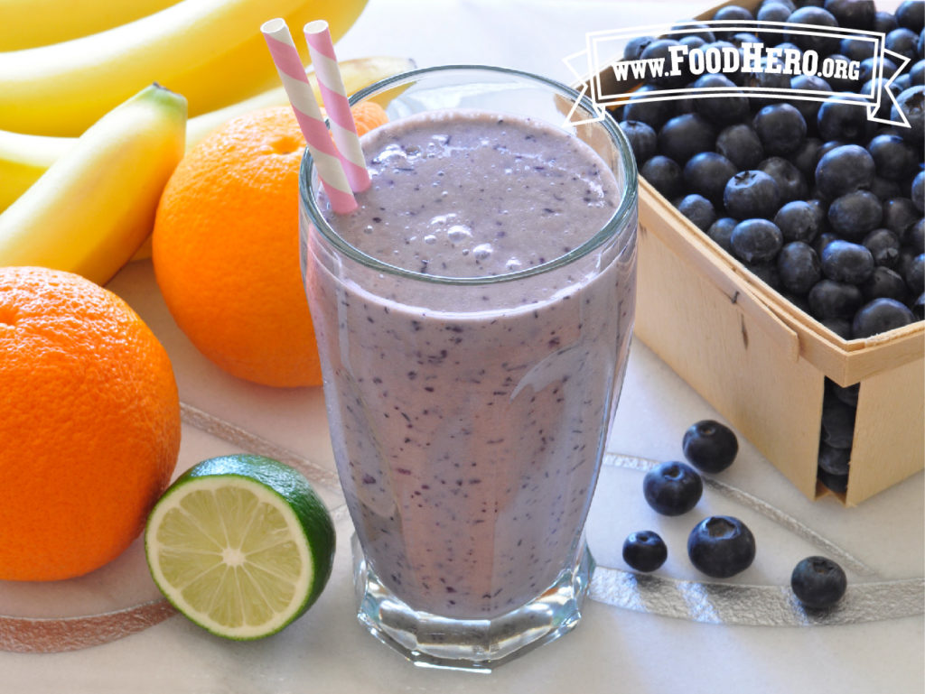 glass of blueberry tofu smoothie with 2 straws next to a box of blueberries