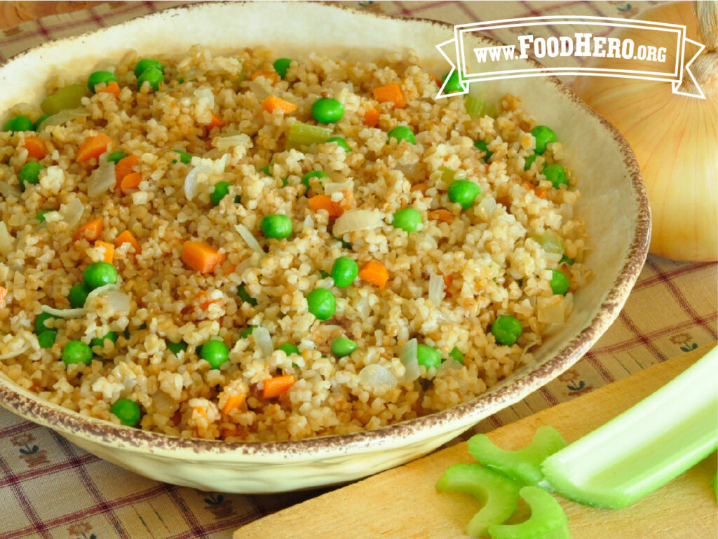 serving bowl of bulgur pilaf next to a cutting board with celery stalk