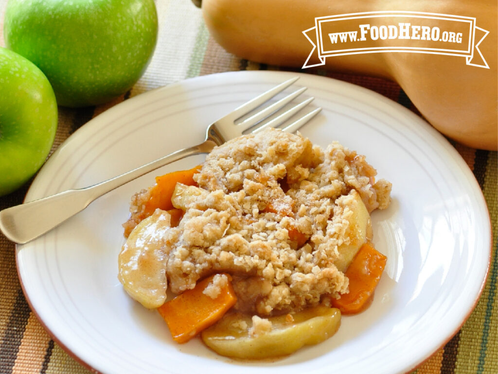plate of butternut apple crisp with fork next to fresh apples and a butternut squash
