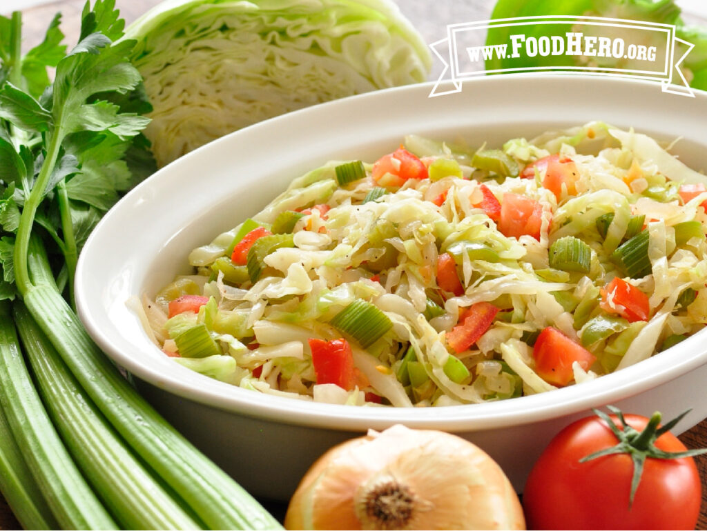 bowl of cabbage stir-fry next to fresh cabbage, celery and onion