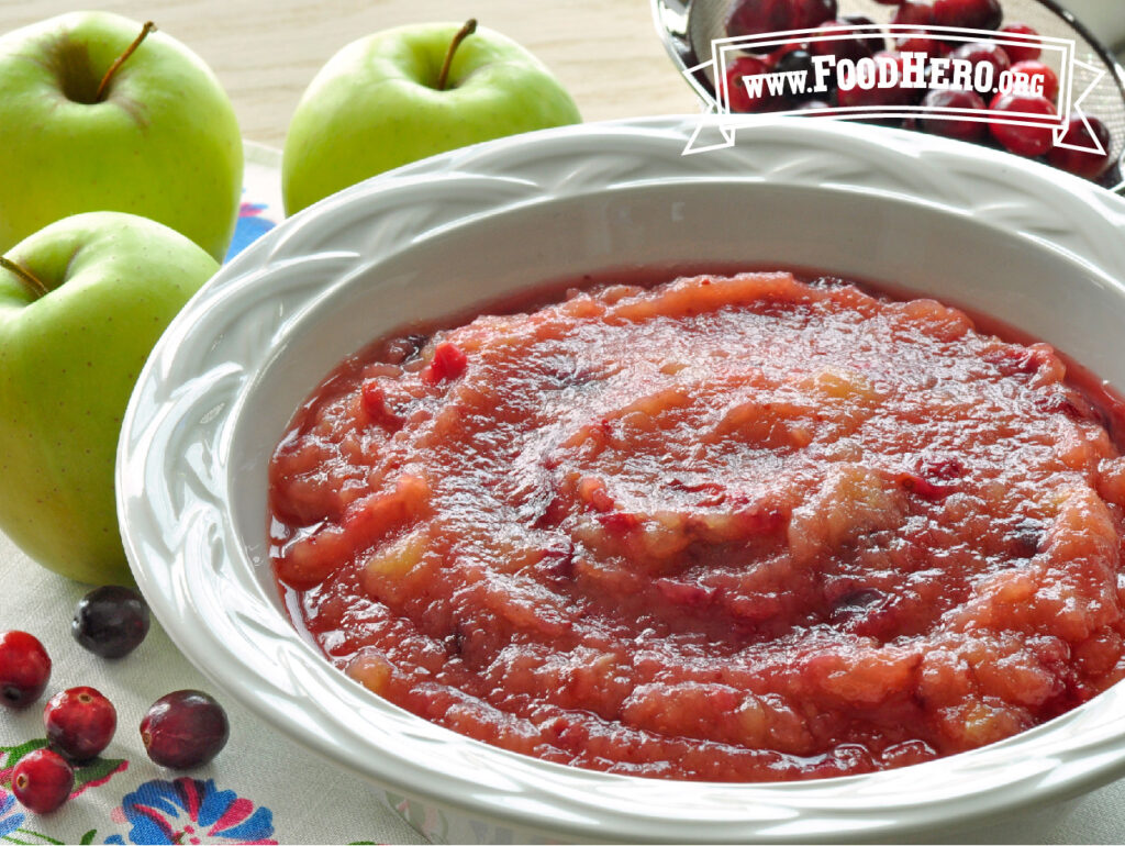 serving bowl of cranberry applesauce next to 3 apples