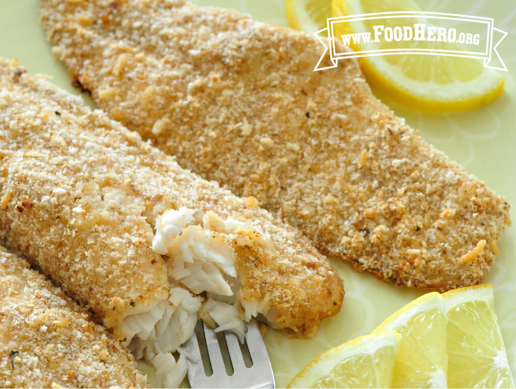 crispy parmesan baked fish with fork and sliced lemons