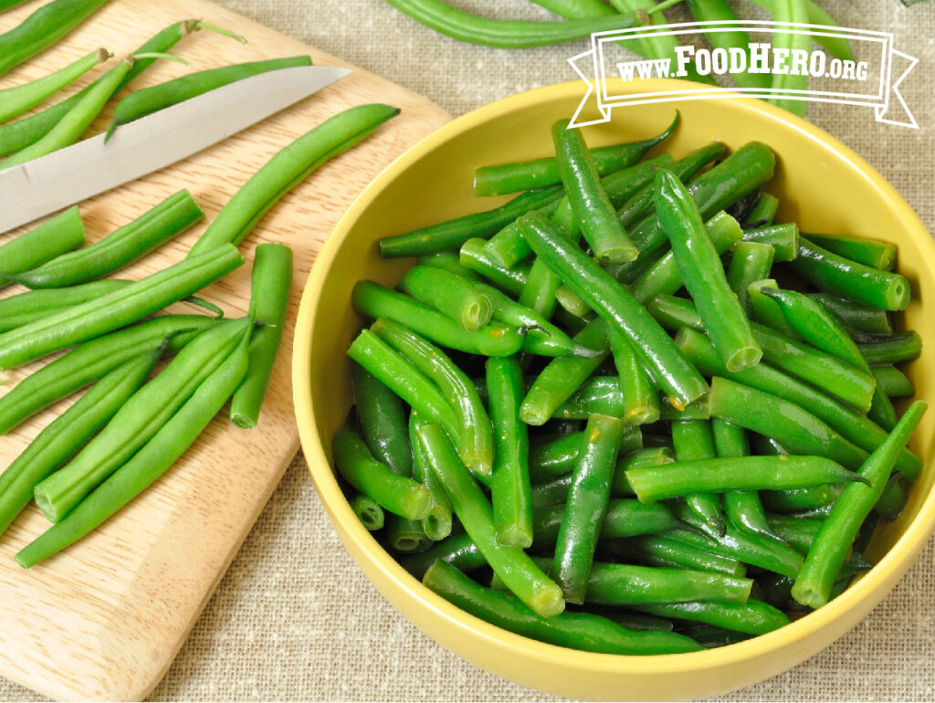 bowl of honey mustard green beans next to chopping board with fresh beans