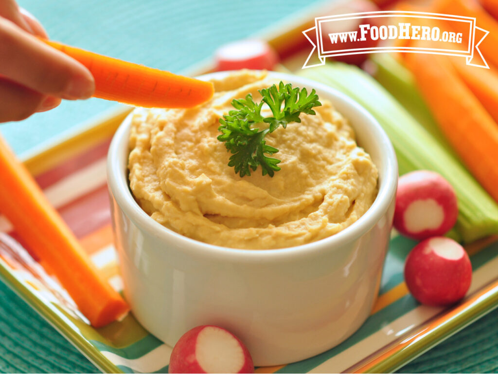 bowl of hummus with tahini with hand dipping carrot stick 