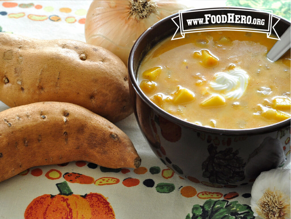 bowl of sweet potato pumpkin soup next to 2 fresh sweet potatoes and an onion