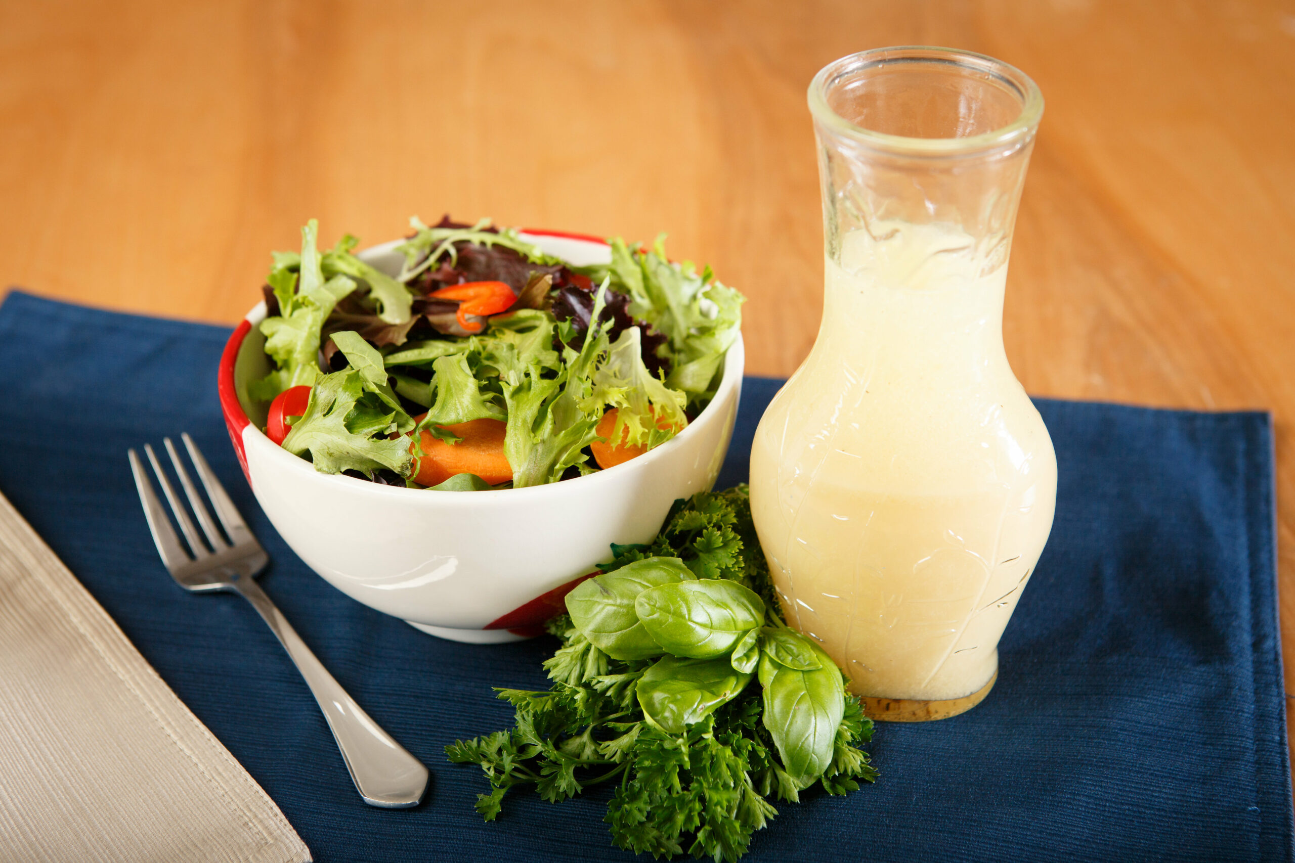 flask containing vinaigrette salad dressing next to salad in a bowl and fork