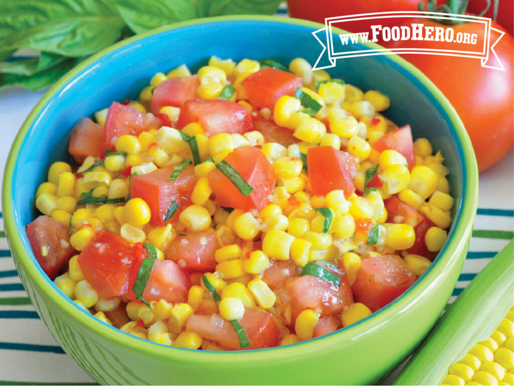 bowl of corn and tomato salad next to fresh corn basil and tomatoes