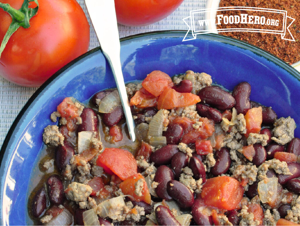 Bowl of easy skillet chili next to fresh tomato and dish of chili powder