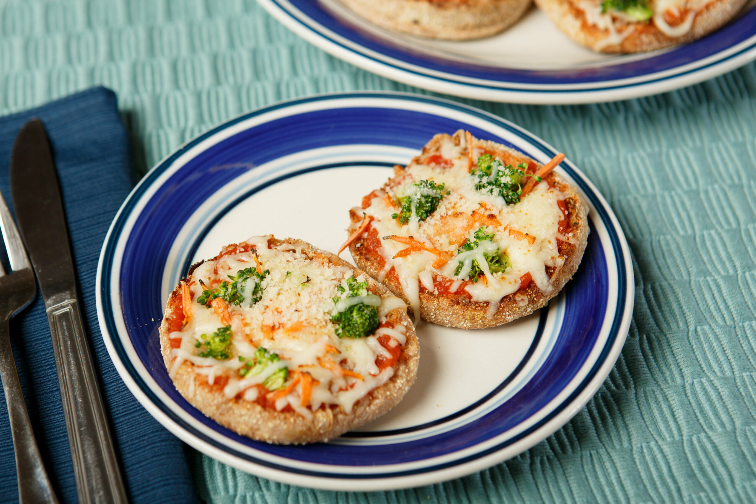 plate with 2 english muffin veggie pizza next to napkin with fork and knife