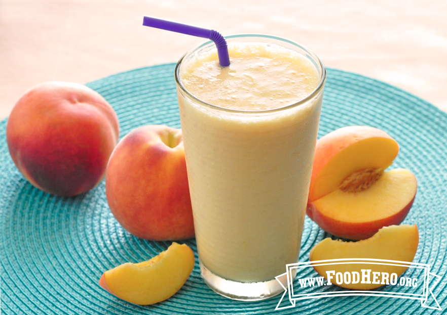 glass of peach cooler next to fresh peaches