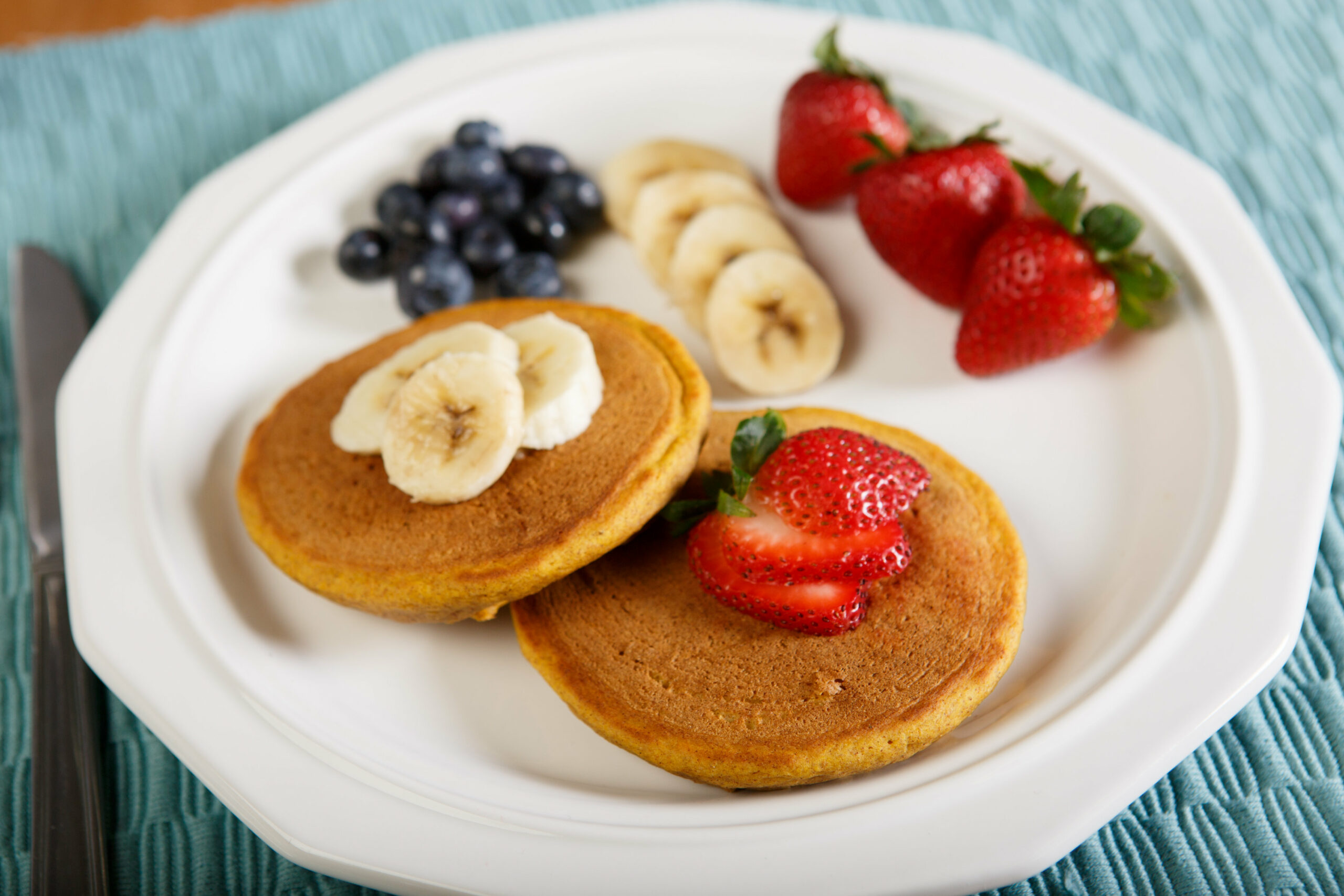 plate of perfect pumpkin pancakes with blueberries , sliced bananas, and strawberries
