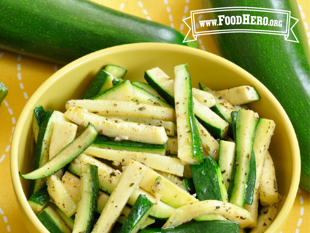 yellow bowl of sauteed zucchini next to 2 fresh zucchinis