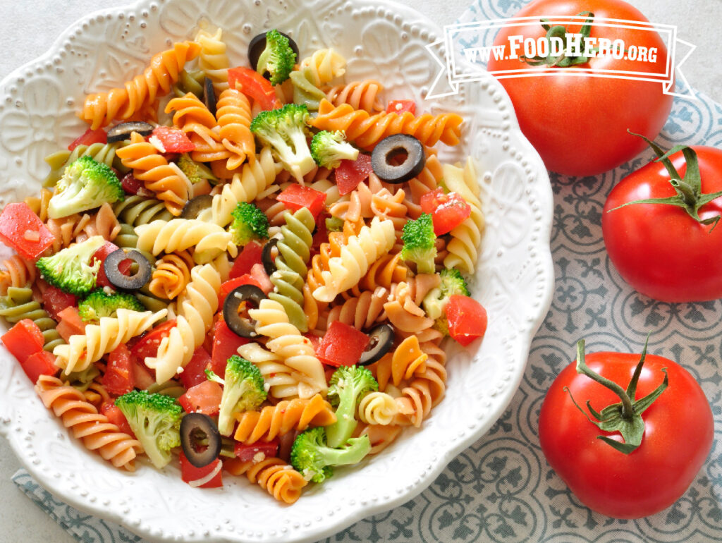 pasta dish of tomato pasta salad next to 3 fresh tomatoes