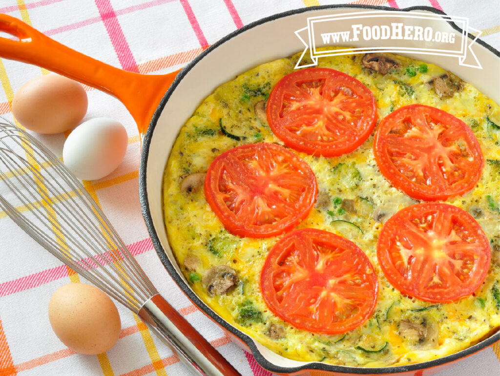 veggie skillet eggs in an orange skilled next to a whisk and 3 eggs