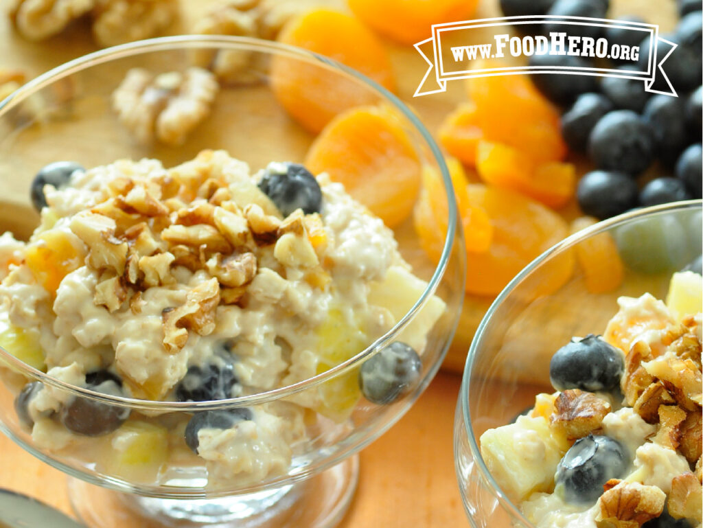 2 glass bowls of very berry muesli next to fresh apricots, blueberries, walnuts 