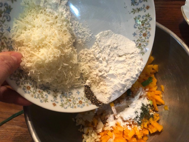 cheese and flour being added to bowl of cut butternut squash